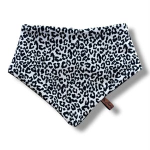 May include: A white and black leopard print bandana with a brown leather tag. The bandana is triangular and has a black border. The leopard print consists of black spots on a white background. The tag has the word "Jane" printed on it.