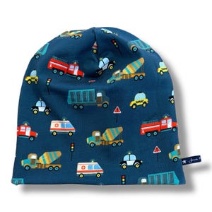 May include: A dark blue beanie hat with a repeating pattern of colourful vehicles, including fire engines, ambulances, cement mixers, and police cars. The hat has a rounded shape and a small tag with text and a star.