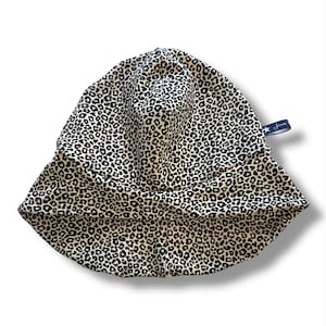 May include: A leopard print sun hat with a wide brim. The hat features a beige background with black spots. A small navy blue tag with white text is attached to the side.