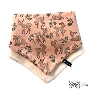 Könnte beinhalten: Ein doppelseitiges Bandana in Rosa und Weiß mit einem Muster aus braunen Rehen und floralen Zweigen. Das Bandana hat ein weißes Fleece-Futter und ein kleines weißes Etikett mit dem aufgedruckten Wort "Juna".