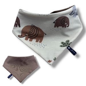 May include: Two bandana bibs, one with a white background and a pattern of brown elephants and green plants, and the other a solid brown color. Both bibs have a small blue tag with the text "Juna & Co."