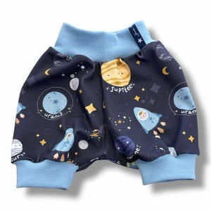 May include: Blue and black baby shorts with a space theme print. The print features planets, stars, and a rocket with the words "Jupiter", "Uranus", and "Mercury".