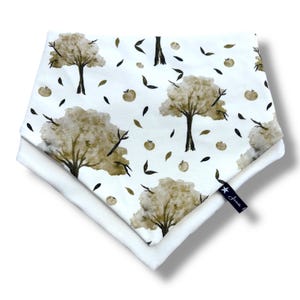 May include: Two white fabric bibs with a brown and green watercolor tree and leaf pattern. The bibs have a white background and feature a small black star with the word "Annie" on the bottom right corner.