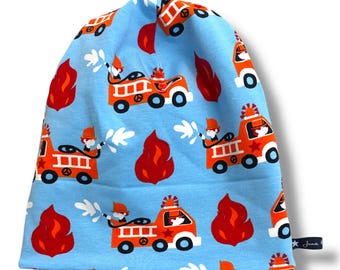 Op de afbeelding: Een lichtblauwe beanie-muts met een herhaald patroon van oranje brandweerwagens, rode vlammen en witte watersproeiers. De muts is gemaakt van een zachte stof en is geschikt voor kinderen.