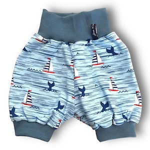 May include: Blue baby shorts with a nautical print featuring sailboats and whale tails. The shorts have a blue elastic waistband and blue cuffs.