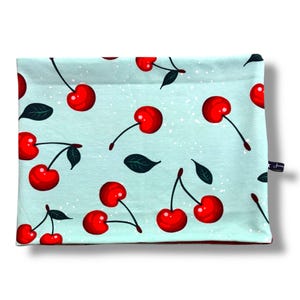 May include: A light blue fabric item with a repeating pattern of bright red cherries and dark green leaves. The cherries have long stems and are scattered across the surface. The item has a small tag on the side.