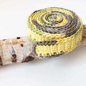 Könnte beinhalten: Ein gehäkeltes Spiralkabel in Gelb- und Grüntönen, das auf einem Stück Birkenrinde liegt.