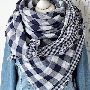 Peut inclure: Un grand foulard carré présentant un motif à carreaux vichy bleu marine et blanc. Le tissu est drapé en plusieurs plis autour d'un mannequin, mettant en valeur un mélange de sections à grands et petits carreaux sur une veste en jean bleue.