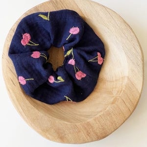 Könnte beinhalten: Ein marineblauer Haargummi mit einem Muster aus rosa und grünen Kirschen.