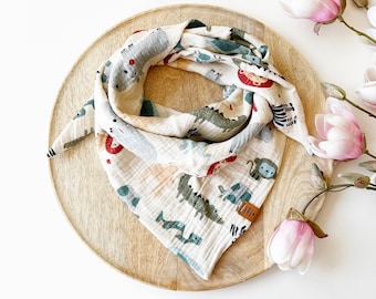 May include: A triangular muslin scarf featuring a cream-coloured background with a repeating pattern of colourful animals including lions, crocodiles, and monkeys. The fabric has a crinkled texture and includes a small brown rectangular brand tag.
