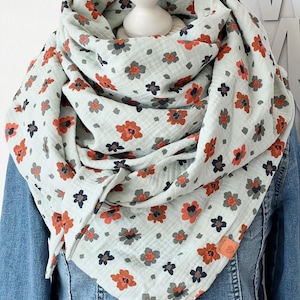 May include: A light blue scarf with a floral pattern featuring orange, gray, and navy flowers. The scarf is draped over a denim jacket, showcasing its soft, flowing fabric and design.