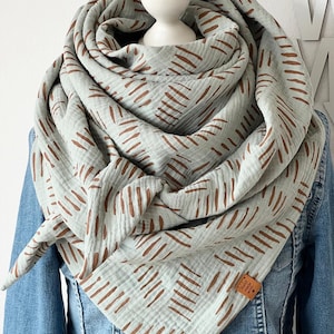 May include: A pale blue scarf with a brown dash pattern is draped around a mannequin head. The scarf is made of a soft, textured fabric and is worn over a denim jacket. A small brown tag is attached to the scarf.