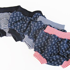 May include: Three pairs of baby bloomers with different patterns. The first pair is striped black and white. The second pair is navy blue with white anchors. The third pair is navy blue with white anchors and a red and white striped waistband.