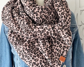 Puede incluir: Una bufanda de estampado de leopardo rosa y marrón con una etiqueta de cuero marrón. La bufanda está doblada y drapeada sobre una chaqueta vaquera.