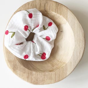 Könnte beinhalten: Ein weißer Haargummi mit roter Kirschen-Stickerei.