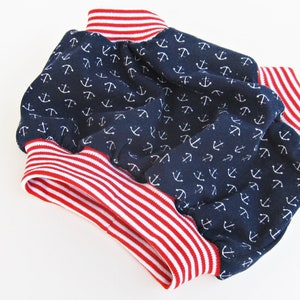 Puede incluir: Un bloomers de beb&eacute; de tela azul marino con estampado de anclas blancas y ribete de rayas rojas y blancas.