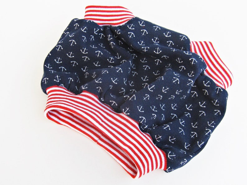 Puede incluir: Un bloomers de beb&eacute; de tela azul marino con estampado de anclas blancas y ribete de rayas rojas y blancas.