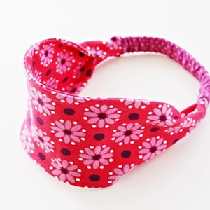 Könnte beinhalten: Ein pinkfarbenes Stirnband mit Blumenmuster. Das Stirnband ist aus Stoff und hat ein elastisches Gummiband.