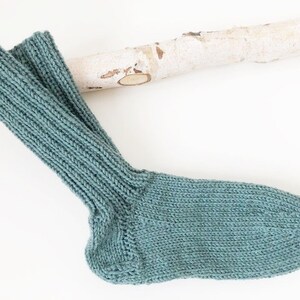 Könnte beinhalten: Ein Paar tealblaue Stricksocken. Die Socken sind mit einem Rippenstrickmuster gefertigt.