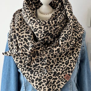 Puede incluir: Una bufanda de estampado de leopardo marrón y negro con una etiqueta de cuero marrón que dice "Made with Love".