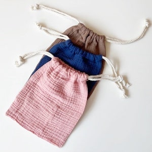 Könnte beinhalten: Drei Kordelbeutel aus weichem, strukturiertem Stoff. Die Beutel sind in rosa, blau und braun.