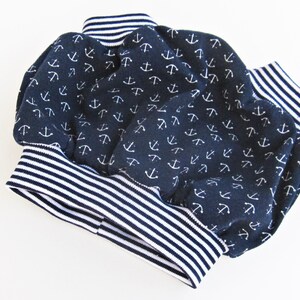 May include: A pair of navy blue baby bloomers with a white anchor print and white and navy blue striped trim.