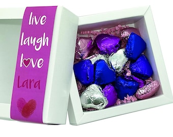 May include: A white gift box with a pink ribbon that says "live laugh love Lara". The box is open and filled with foil-wrapped chocolate hearts in pink, blue, and silver.