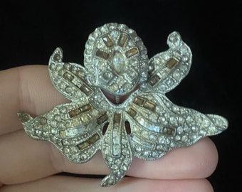 May include: A silver-toned brooch in the shape of a flower with clear and brown rhinestones.