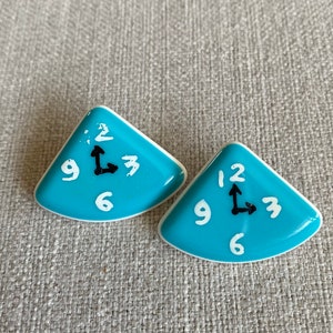 May include: Two turquoise blue ceramic clock earrings with white numbers and black hands. The hands point to 12 and 3.