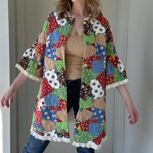 May include: A patchwork jacket with a colorful mix of red, blue, green, and white fabric squares. The jacket has a collarless design, three-quarter sleeves, and is trimmed with white lace. The jacket is worn over a neutral top and blue jeans.