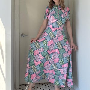 May include: A patchwork maxi dress in pink, green, and blue. The dress has a collared neckline, short sleeves, and a button-down front. The fabric appears lightweight. The dress has a fitted waist and a flowing skirt. The dress is suitable for warmer weather.