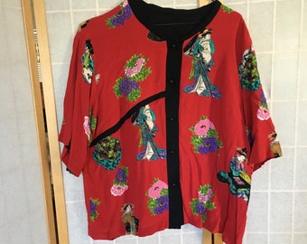 Pode incluir: Uma camisa vermelha de manga curta com botões, colarinho preto e estampa floral com geishas. A camisa tem um design único com um painel preto na frente.