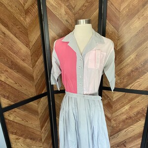 Könnte beinhalten: Ein Kleid im Vintage-Stil in einem hellblauen, rosa und weißen Farbschema. Das Kleid hat einen Kragen, eine Knopfleiste vorne und einen Faltenrock.