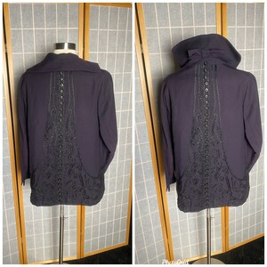 Puede incluir: Una chaqueta de color morado oscuro con un dise&ntilde;o bordado en negro en la espalda. La chaqueta tiene un cuello alto y cierre de botones.