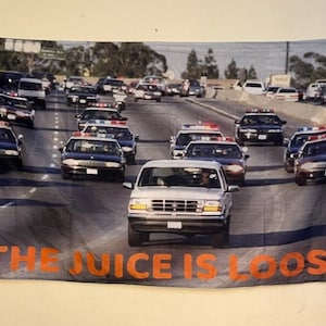 May include: A black and white flag with a photo of a white Ford Bronco surrounded by police cars on a highway. The text "THE JUICE IS LOOSE" is printed in orange at the bottom of the flag.