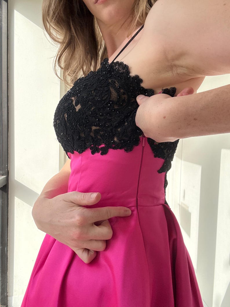Pu&ograve; includere: Un abito da sera rosa acceso con corpetto in pizzo nero. L'abito ha un corpetto aderente e una gonna svasata. Il pizzo nero &egrave; impreziosito da piccole perline scure. L'abito &egrave; senza maniche con sottili spalline.