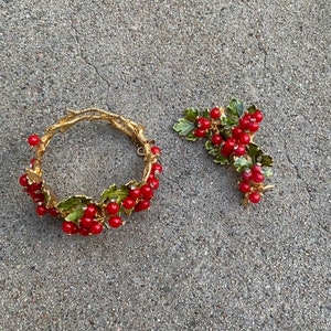 May include: A gold bracelet and brooch set with red berries and green leaves. The jewelry is made of metal and has a vintage style.