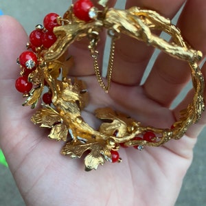 May include: Gold tone bracelet with red and clear rhinestones, featuring a leafy design with a chain detail.