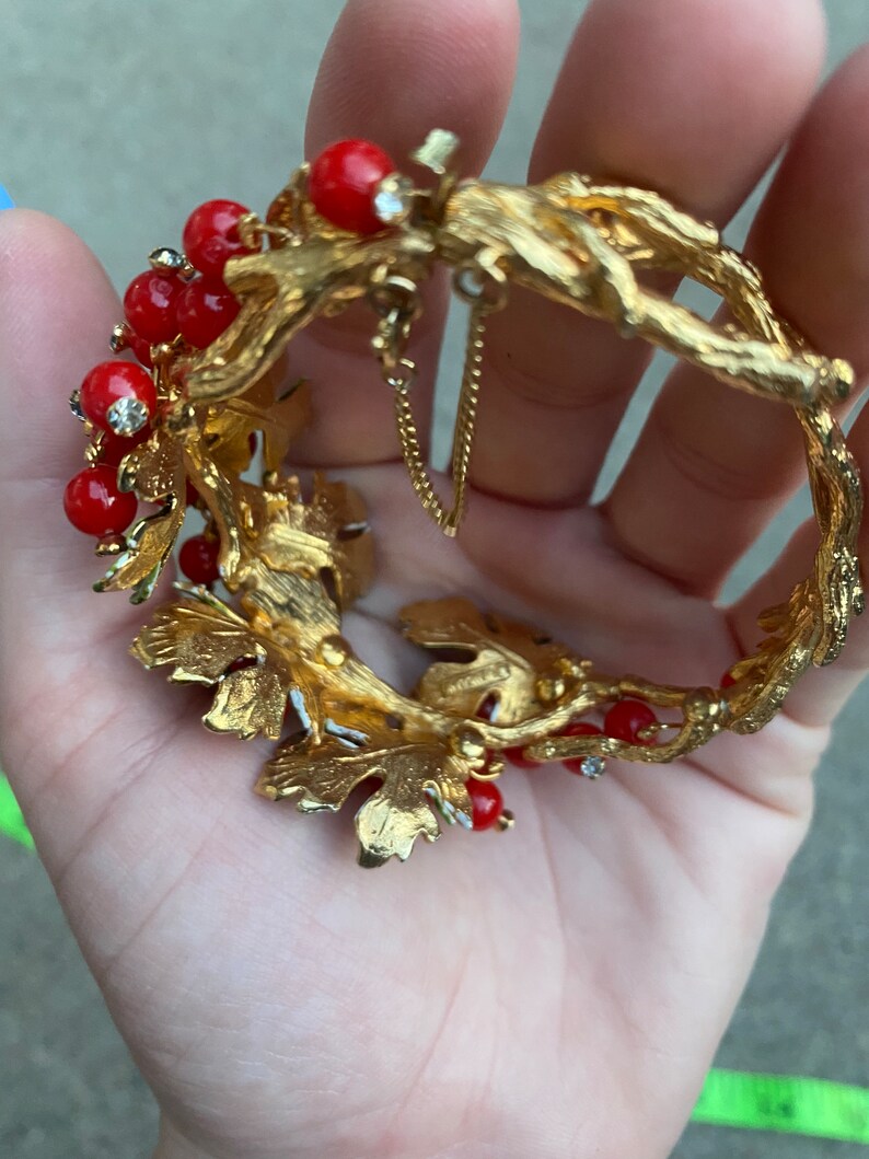 May include: Gold tone bracelet with red and clear rhinestones, featuring a leafy design with a chain detail.