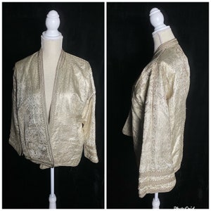 May include: A gold brocade jacket with a long, open front and three-quarter sleeves. The jacket has a paisley pattern and is trimmed with a gold braid.