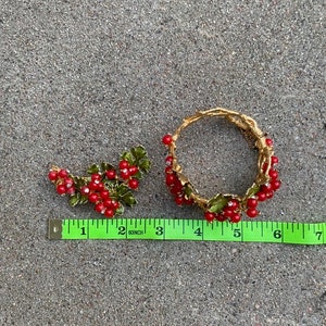 May include: A gold-tone bracelet and brooch set with red and green enamel berries. The bracelet is 6 inches in diameter and the brooch is 2 inches long.