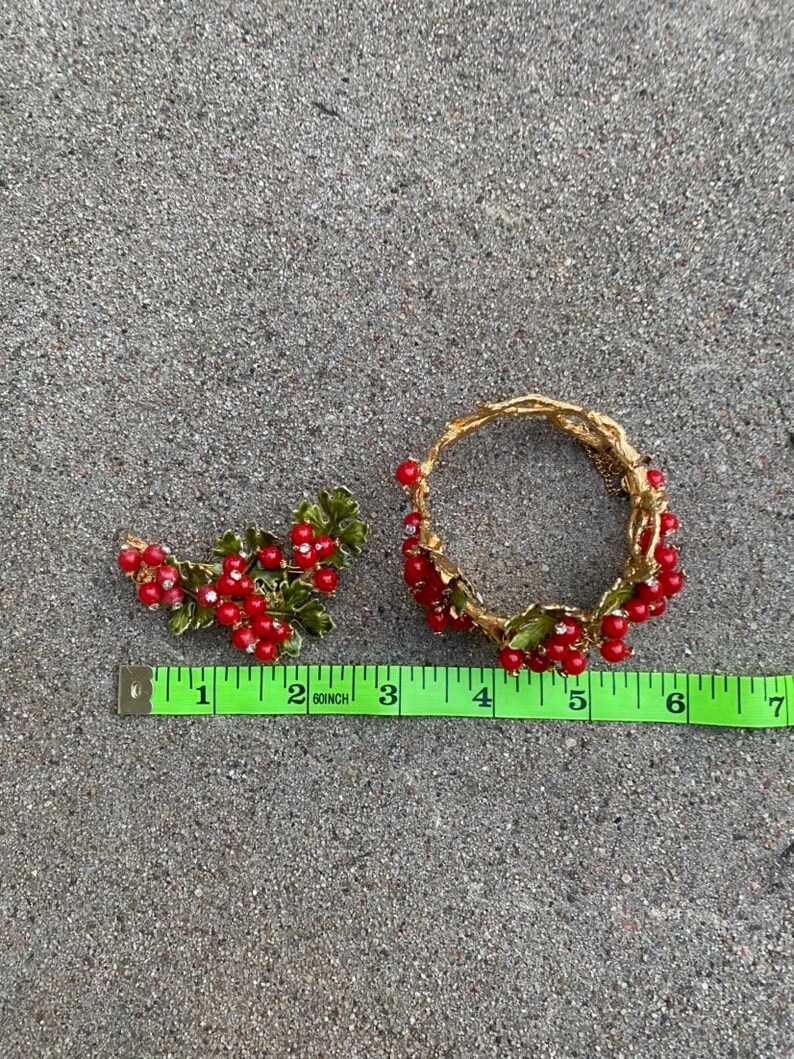 May include: A gold-tone bracelet and brooch set with red and green enamel berries. The bracelet is 6 inches in diameter and the brooch is 2 inches long.