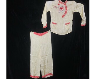 May include: A two-piece pajama set in a pale yellow color with red trim. The top has a mandarin collar and long sleeves. The pants have a straight leg. The top has the name "Kitty" embroidered on the front.