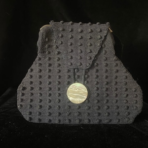 May include: A black crocheted handbag with a round, white, mother-of-pearl button.