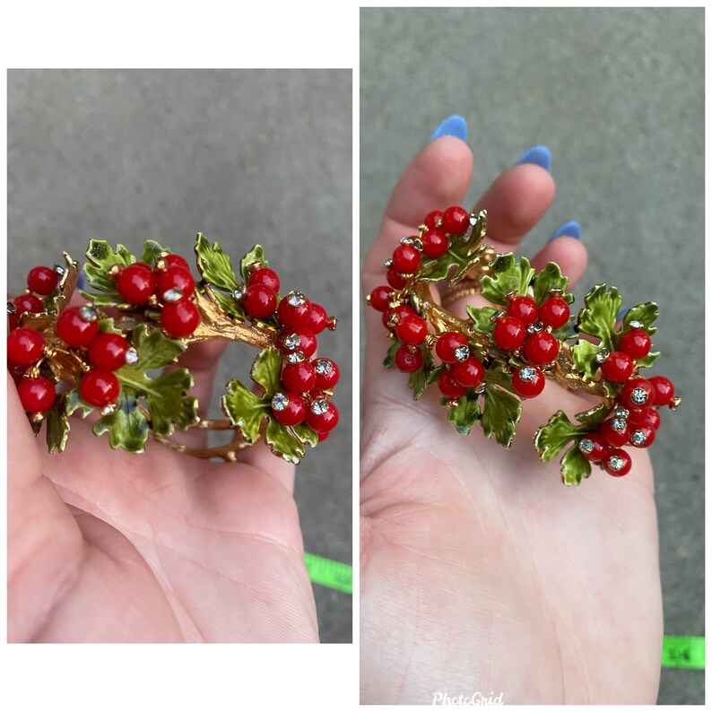 May include: A gold-tone bracelet with red and green enamel. The bracelet is shaped like a branch with red berries and green leaves. The berries have small clear rhinestones.