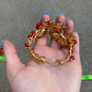 May include: Gold tone bracelet with red glass beads and gold leaf accents. The bracelet is open and has a delicate, twig-like design.
