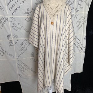 May include: A white and gray striped poncho with a crocheted collar and fringe trim. The poncho is made of a soft, warm material and has a button closure.