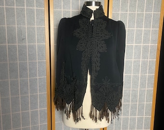 May include: A black velvet jacket with intricate embroidery and brown fringe trim. The jacket has a high collar and a button closure.