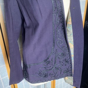 Puede incluir: Una chaqueta de color morado oscuro con un dise&ntilde;o bordado en negro en la parte delantera. El bordado es un patr&oacute;n floral con detalles intrincados.
