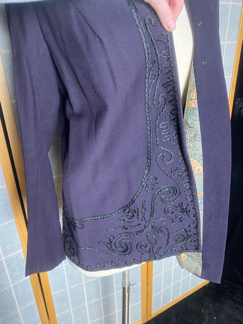 Puede incluir: Una chaqueta de color morado oscuro con un dise&ntilde;o bordado en negro en la parte delantera. El bordado es un patr&oacute;n floral con detalles intrincados.